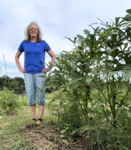 Nancy standing in her pickle patch garden next to her okra plants