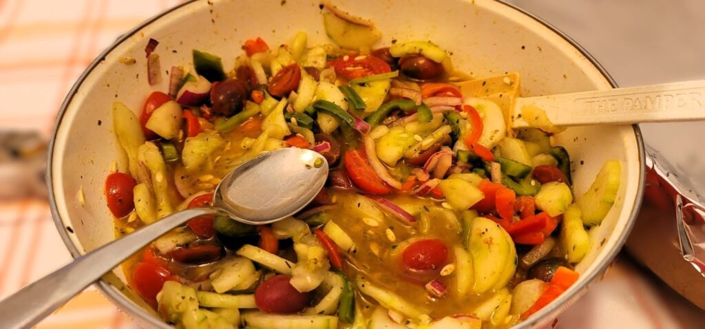 In a bowl are Green and Red Tomatoes, cucumbers and bell peppers salad. the serving tools are also showing.