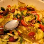 In a bowl are Green and Red Tomatoes, cucumbers and bell peppers salad. the serving tools are also showing.